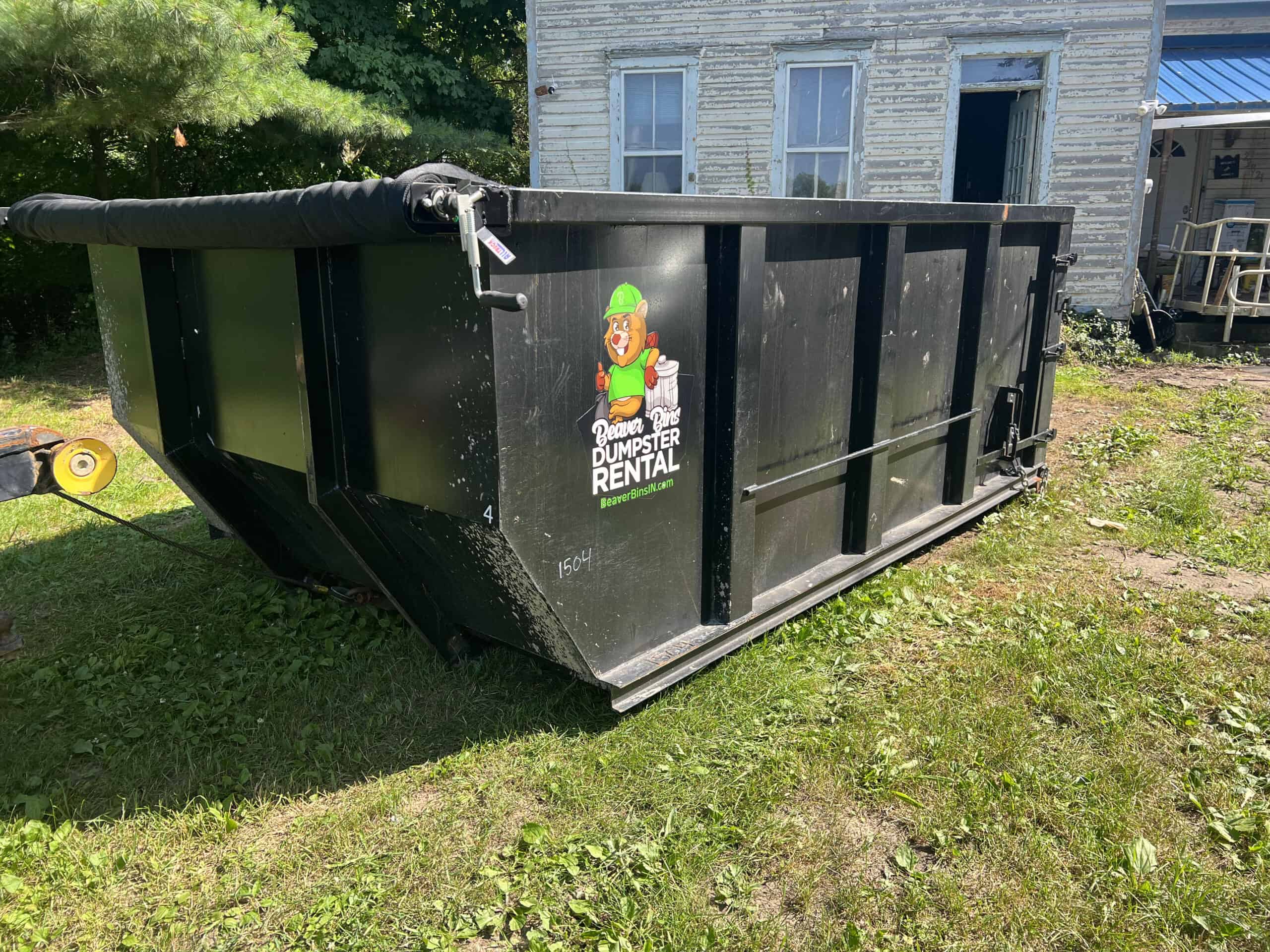 a black Beaver Bins dumpster sitting outside an old house